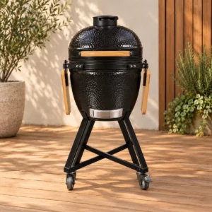 Barbecue kamado 23,5 pouces noir, avec tablettes en bois rabattues et chariot à roulettes.